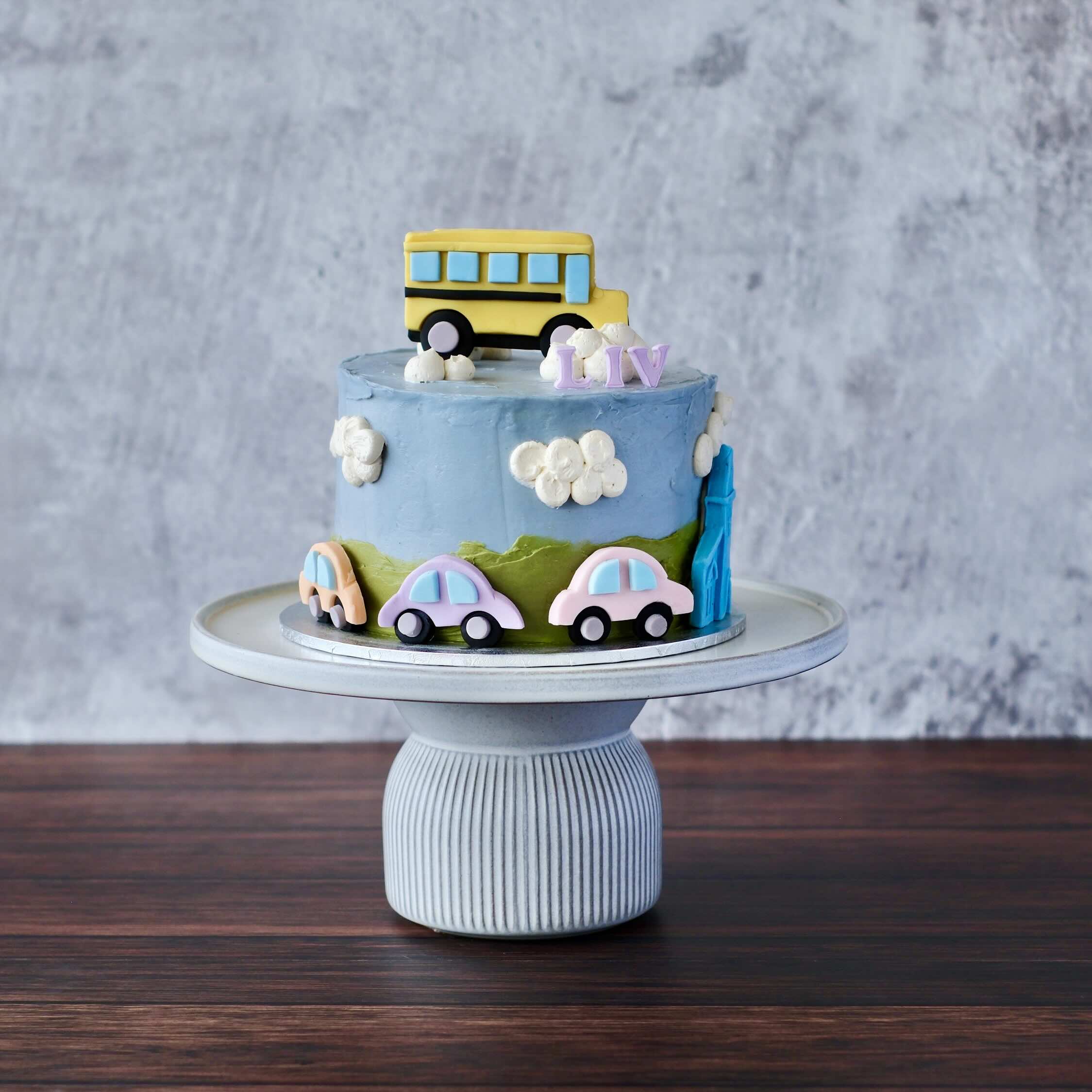kids birthday cake with blue buttercream, fondant bus and cars, cloud details and personalised name, styled for a playful one-year celebration.
