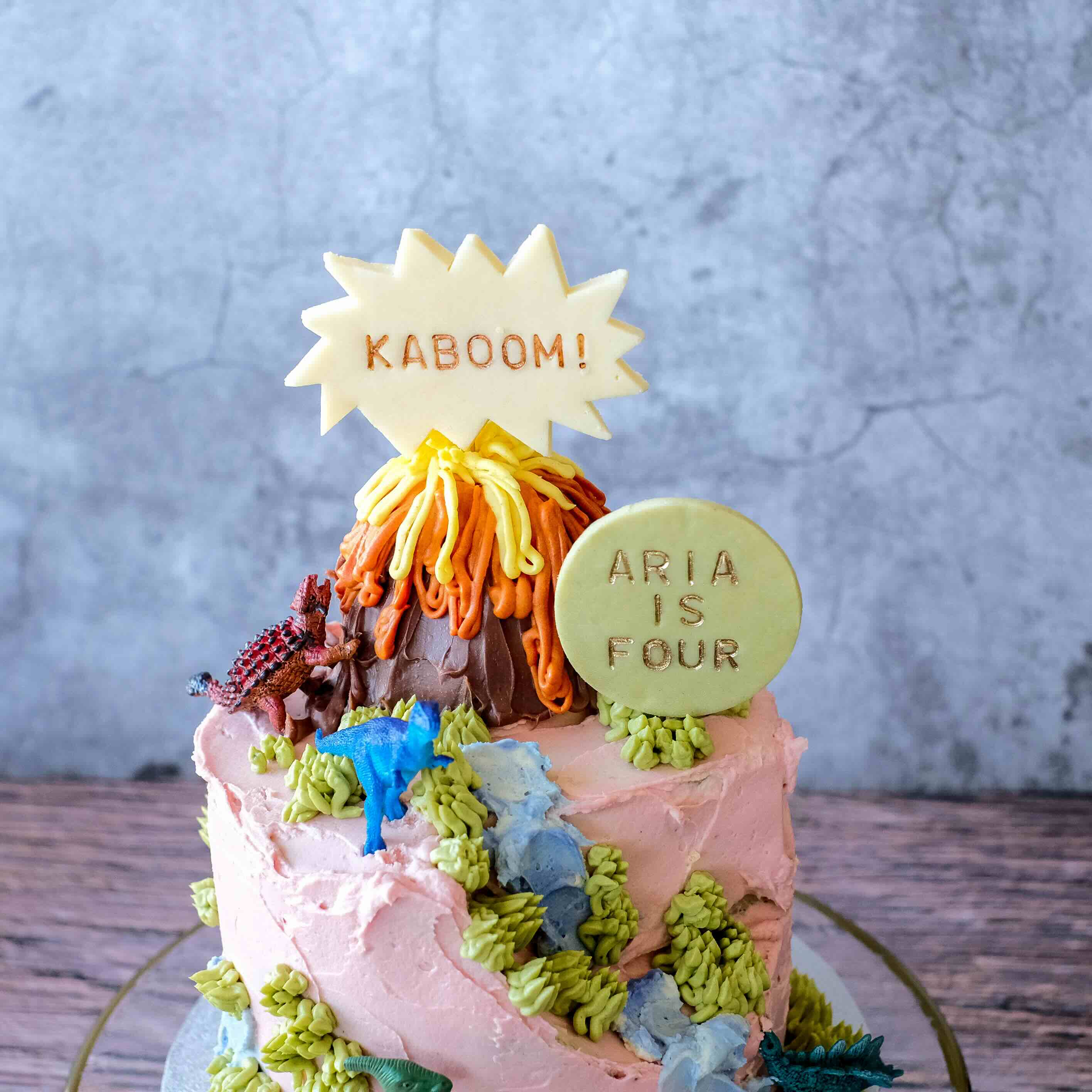 Children's birthday cake featuring a close up of a volcano, a lake and toy dinosaurs in Perth, Western Australia