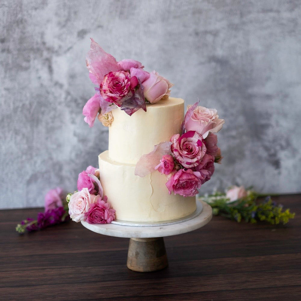 Two-tiered cake decorated with pink and purple flowers perfect for celebrating a baby shower.