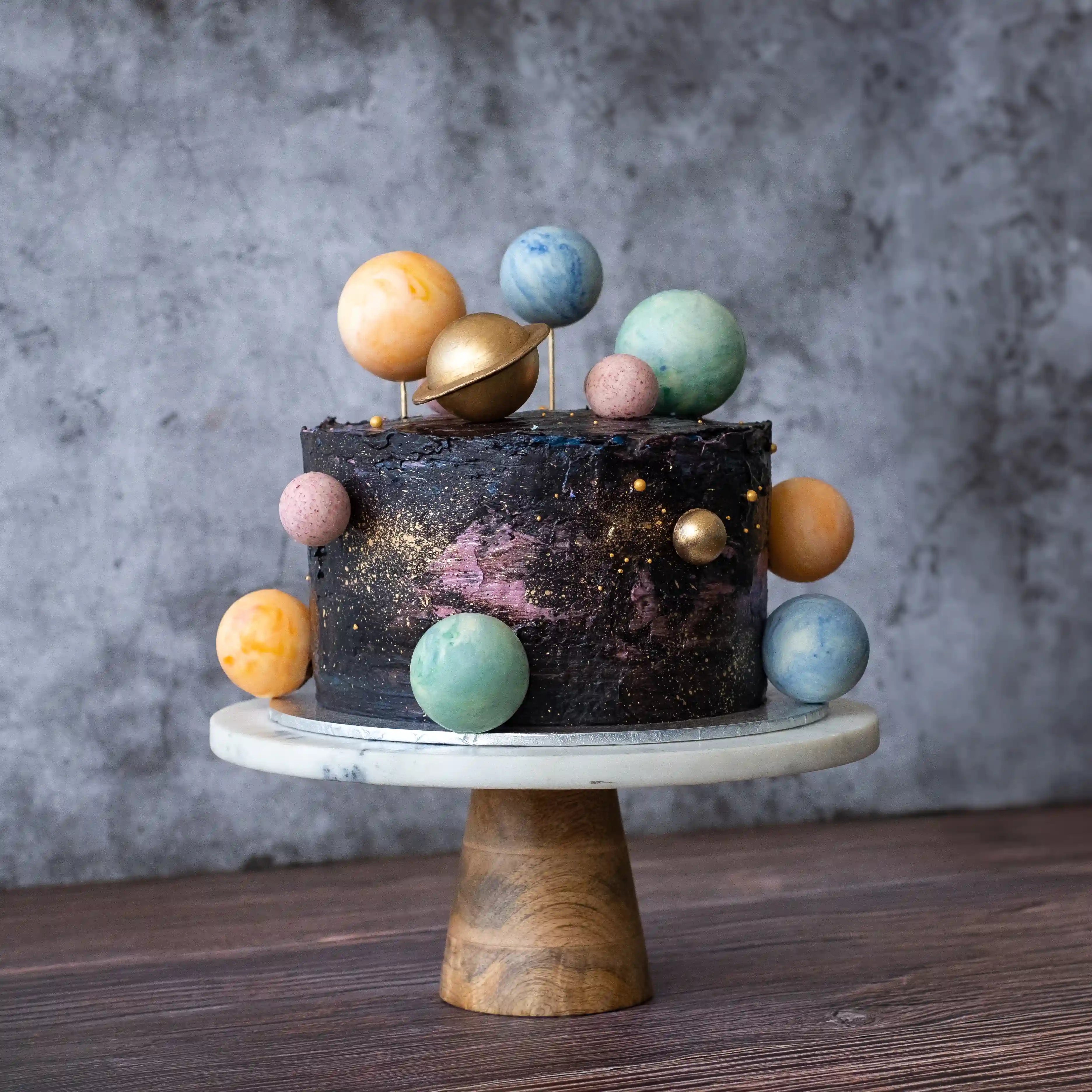 Planet-themed celebration cake with dark galaxy buttercream, hand-painted space details, and colourful fondant planets orbiting the cake.