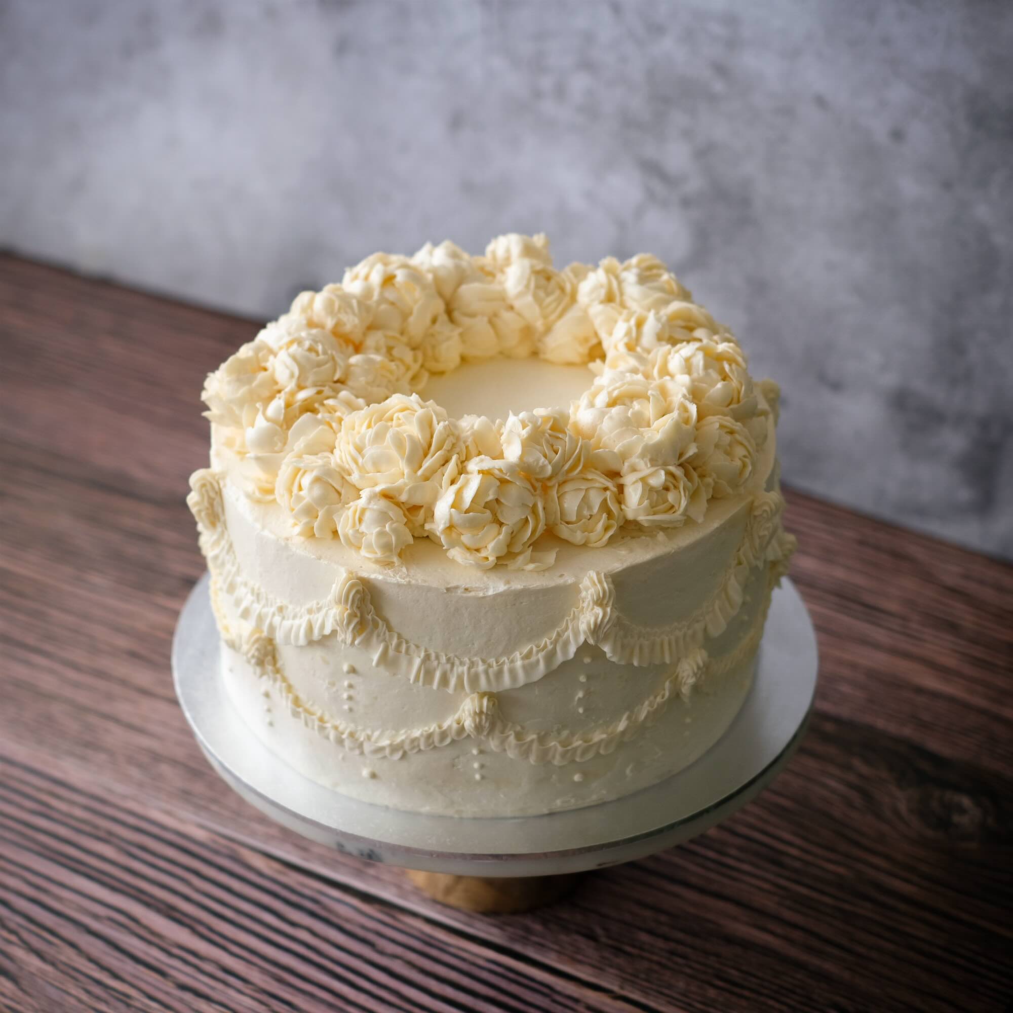 Elegant ivory buttercream cake with piped floral rosettes and delicate vintage-style detailing, for a minimalist wedding or a birthday celebration.