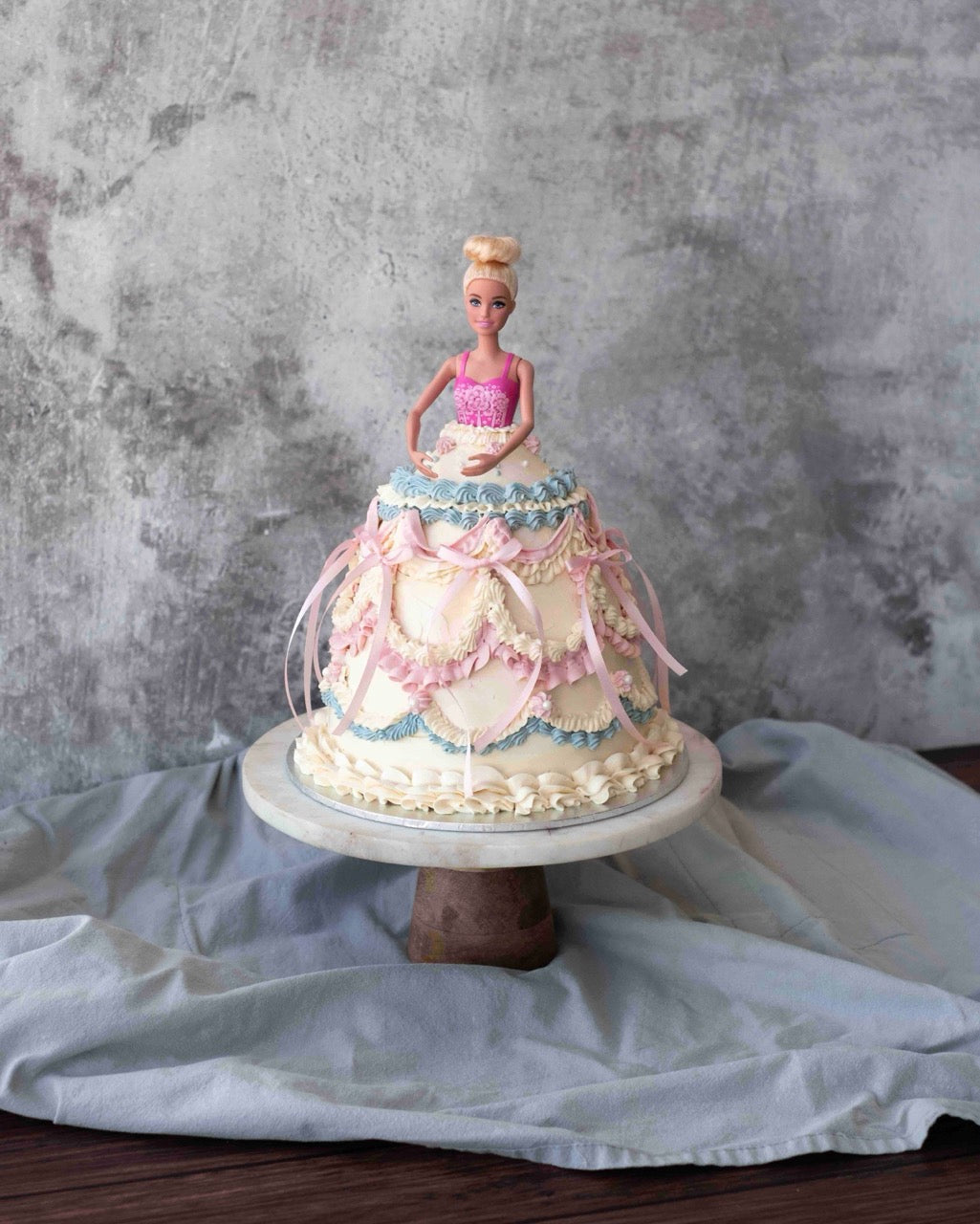 Doll dress cake with layered buttercream gown, soft pastel piping and ribbon details, styled as an elegant birthday celebration cake.