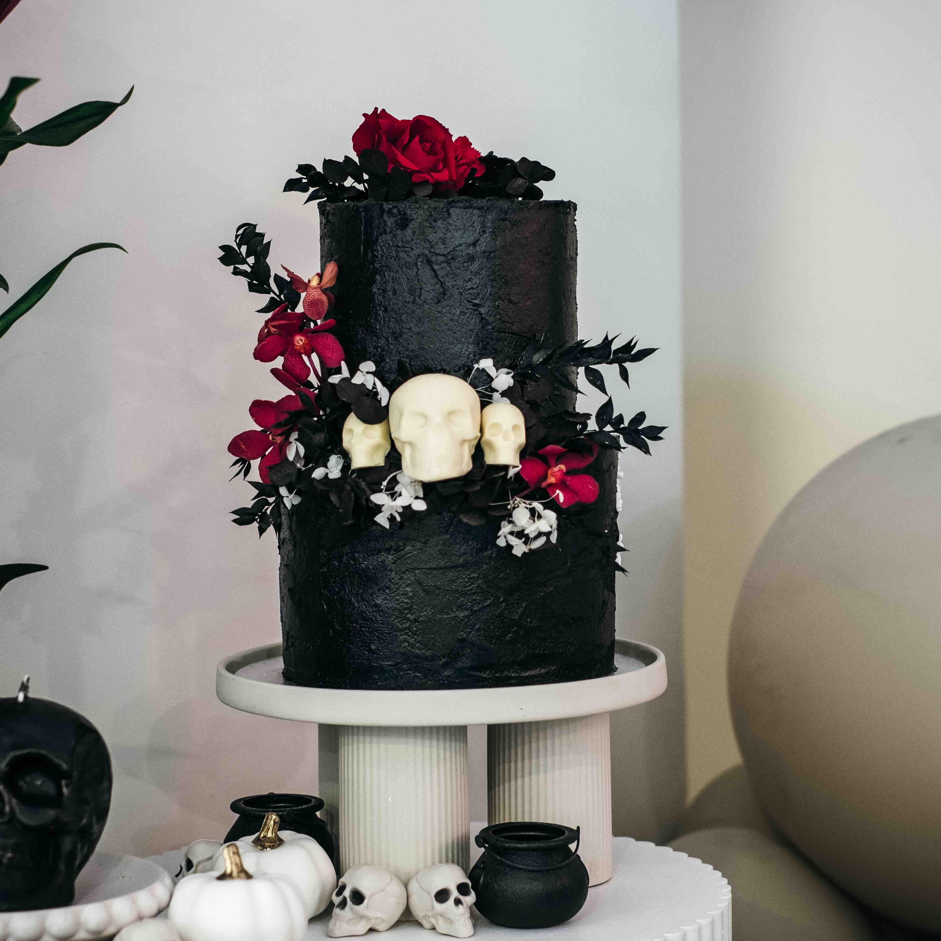 Two Tier cake with black icing, black-red flower arrangement and decorated with white chocolate skulls.