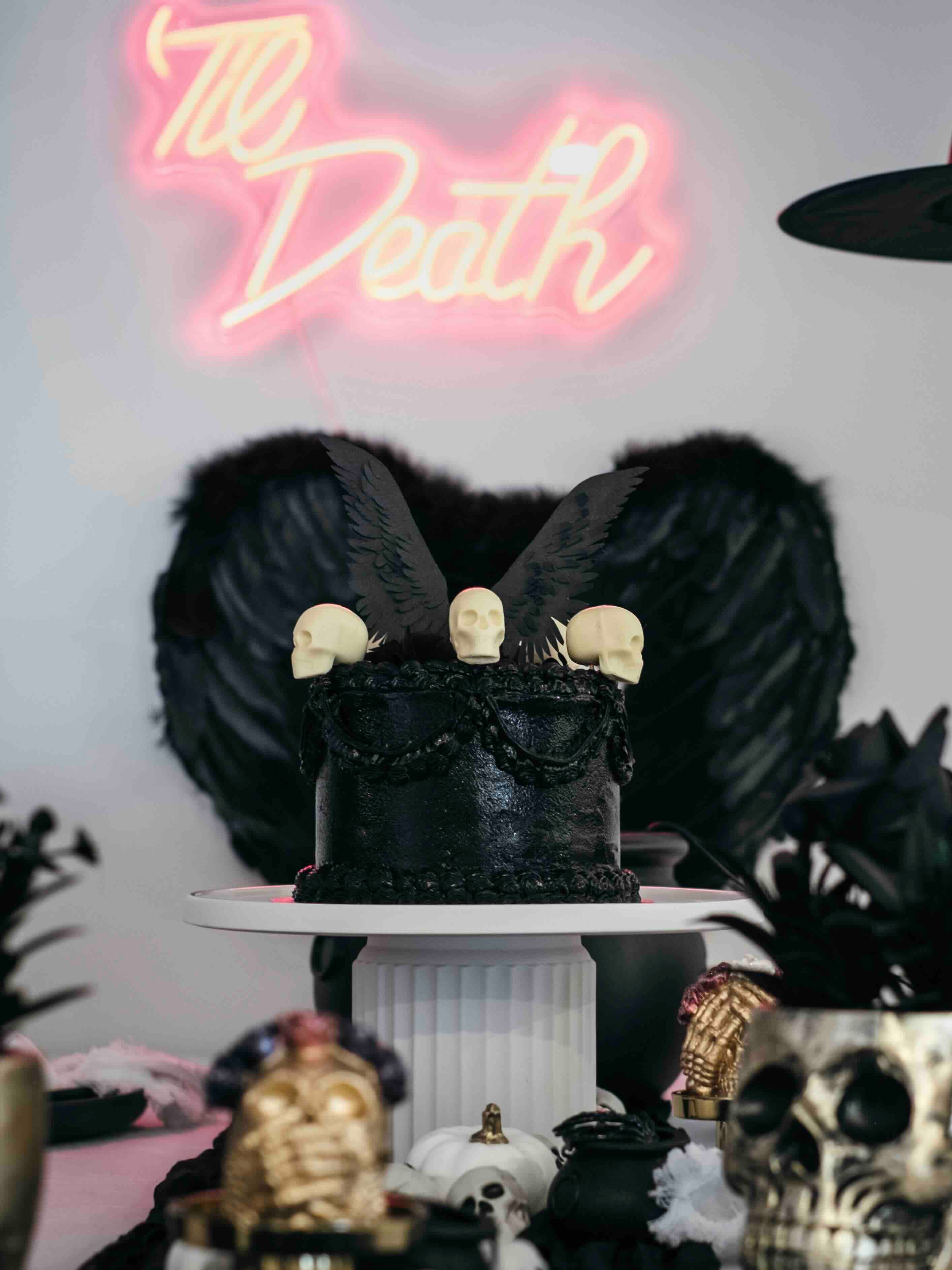 A Gothic Wedding Cake styled with white chocolate edible skulls and a set of black winged cake topper and vintage style piped buttercream.