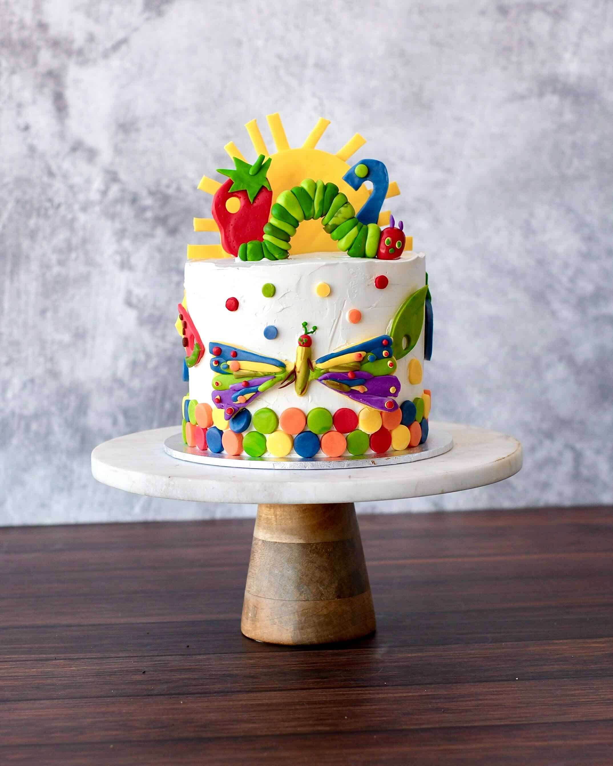 Hungry Caterpillar themed birthday cake with colourful fondant caterpillar, sun, butterfly and bright details, styled for a playful children’s celebration.